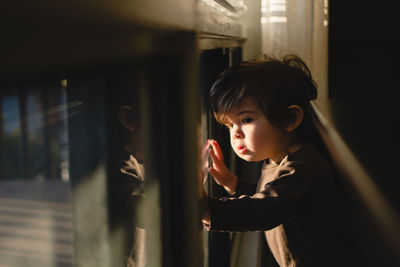 Close-up portrait of young boy looking through window