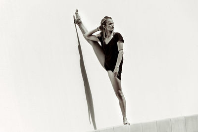 Woman stretching legs against wall in sunny day