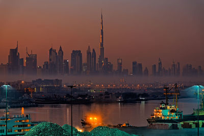 Illuminated buildings by sea at dusk