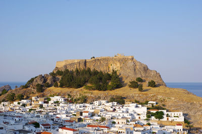 Buildings by sea against clear blue sky