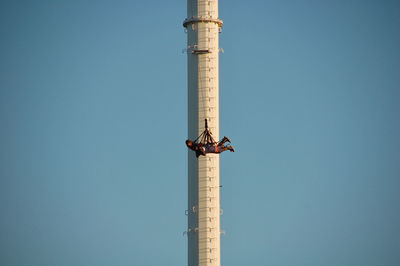 People hanging from tower against clear blue sky