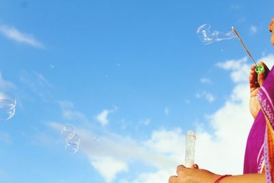 Low angle view of hand holding bubbles against sky