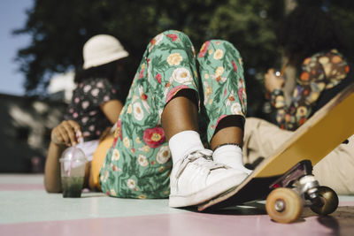 Young non-binary person lying down with skateboard and friends in park during sunny day