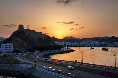 Cars on street by city against sky during sunset