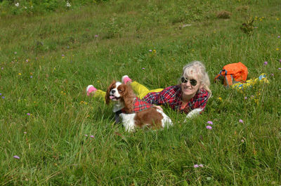 Woman dressed in rustic royal stewart shirt, lying on green meadow resting with her pet