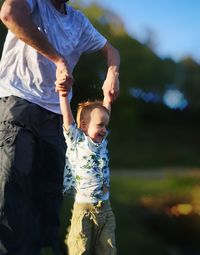 Midsection of father holding son hands in park