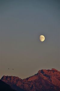 Low angle view of moon in mountains against sky at night