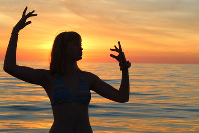 Woman standing by sea against sky during sunset