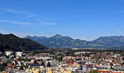 Aerial view of townscape and mountains against blue sky