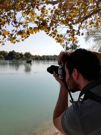 Portrait of man photographing by lake