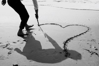 Low section of person making heart shape on wet shore