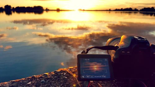 Close-up of camera on sea against sky during sunset