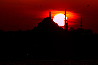 Silhouette of temple against building during sunset