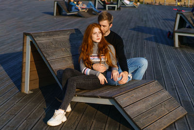 Young woman using phone while sitting on wood