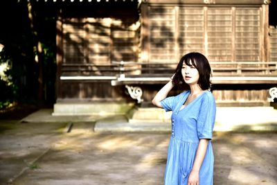 Portrait of young woman standing against building