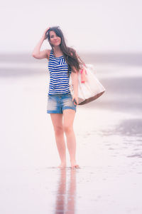 Full length of young woman standing on shore at beach