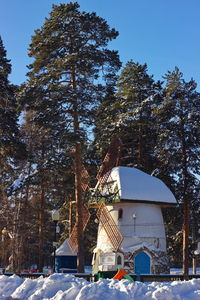 Snow covered trees by building against sky during winter