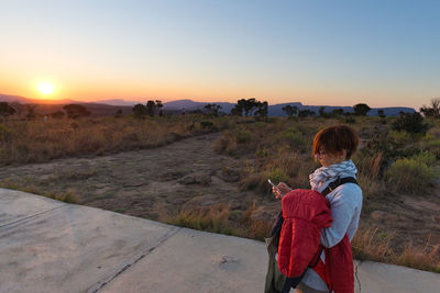 Woman using mobile phone while standing on footpath during sunset