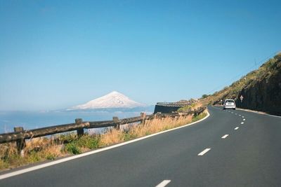 Country road leading towards mountains against blue sky
