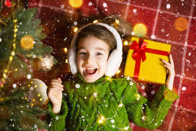 Portrait of cute cheerful girl holding christmas gift lying on bed