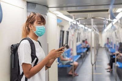 Young asian backpacker woman wear face mask holding smartphone travel subway or skytrain