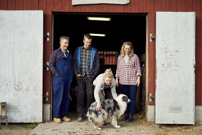 Family looking at teenage girl stroking australian shepherd while standing at doorway of barn