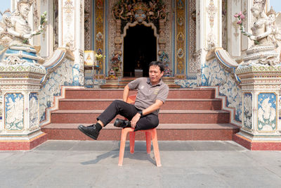 Full length of smiling young woman sitting on chair outside temple