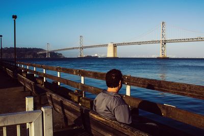 Rear view of man looking at suspension bridge against sky