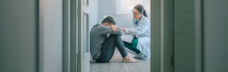 Doctor reassuring and helping to patient sitting on room floor
