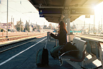 Side view of mature woman with luggage sitting at railroad station platform