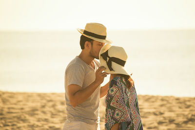 Man kissing on woman forehead at beach against sky