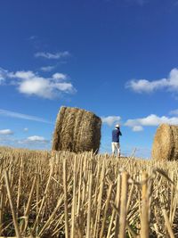Man standing on hay bales in field against sky