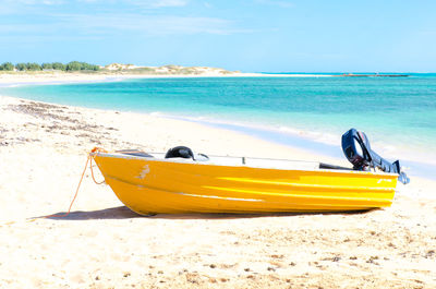 Yellow boat moored on beach against sky