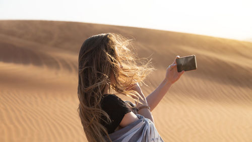 Rear view of woman using mobile phone against sky