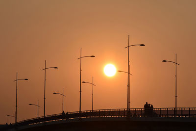 Silhouettes of people walking over the bridge from one side to another at sunset