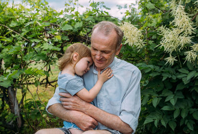 A little girl hugs her grandfather on a walk in the summer outdoors.