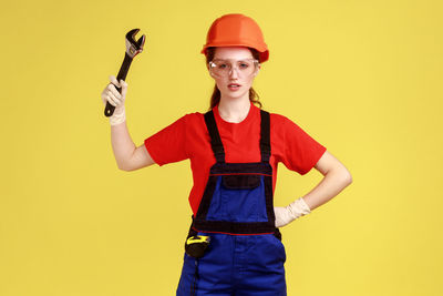 Portrait of young woman holding wrench against yellow background