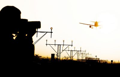 Silhouette man photographing airplane against sky