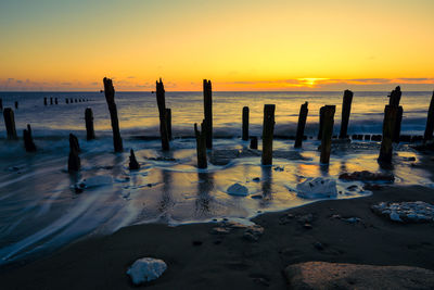 Wooden posts at beach against sky during sunset