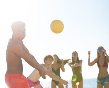 People playing with ball on beach against clear sky