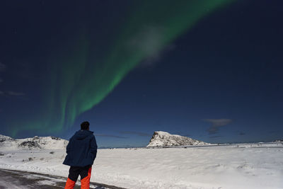 Rear view of man standing on snow watching aurora