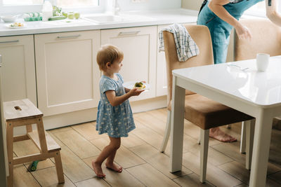 Mom and little daughter are setting the table for dinner at home in the kitchen.