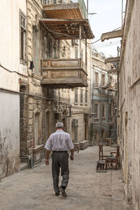 Rear view of man walking on street amidst buildings