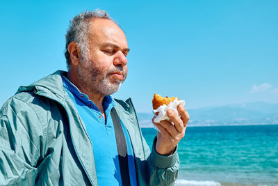 Bearded mature man at spring seaside eating hot palatable arancina