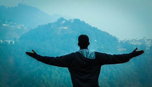 Rear view of man standing with arms outstretched against mountains