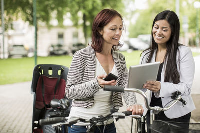 Happy businesswomen with bicycles using digital tablet on street