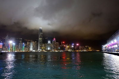 Illuminated buildings by river against sky at night