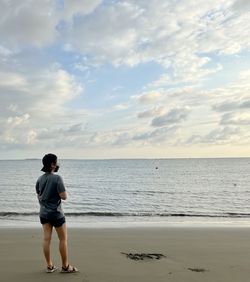 Rear view of woman standing at beach against sky during sunset