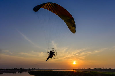 Person paragliding against sky during sunset