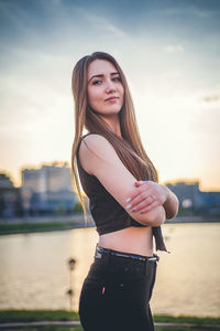 Portrait of beautiful woman with arms crossed standing by lake